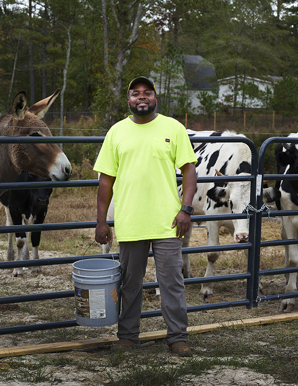 Black Farmer giving livestock feed by Alison Gootee Photography